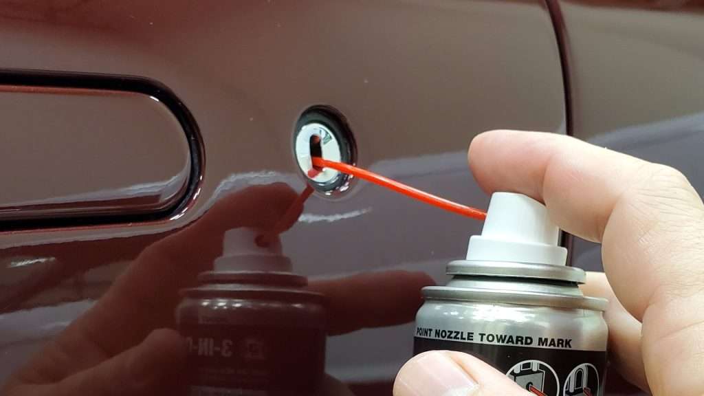 An owner spraying lubricant on the door lock keyway as part of car lock maintenance