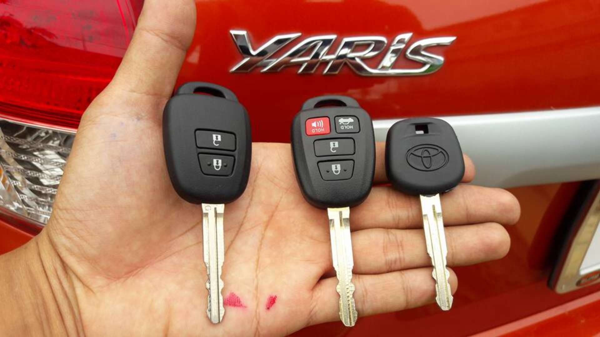 A locksmith holding different Toyota key replacement options for the Yaris model